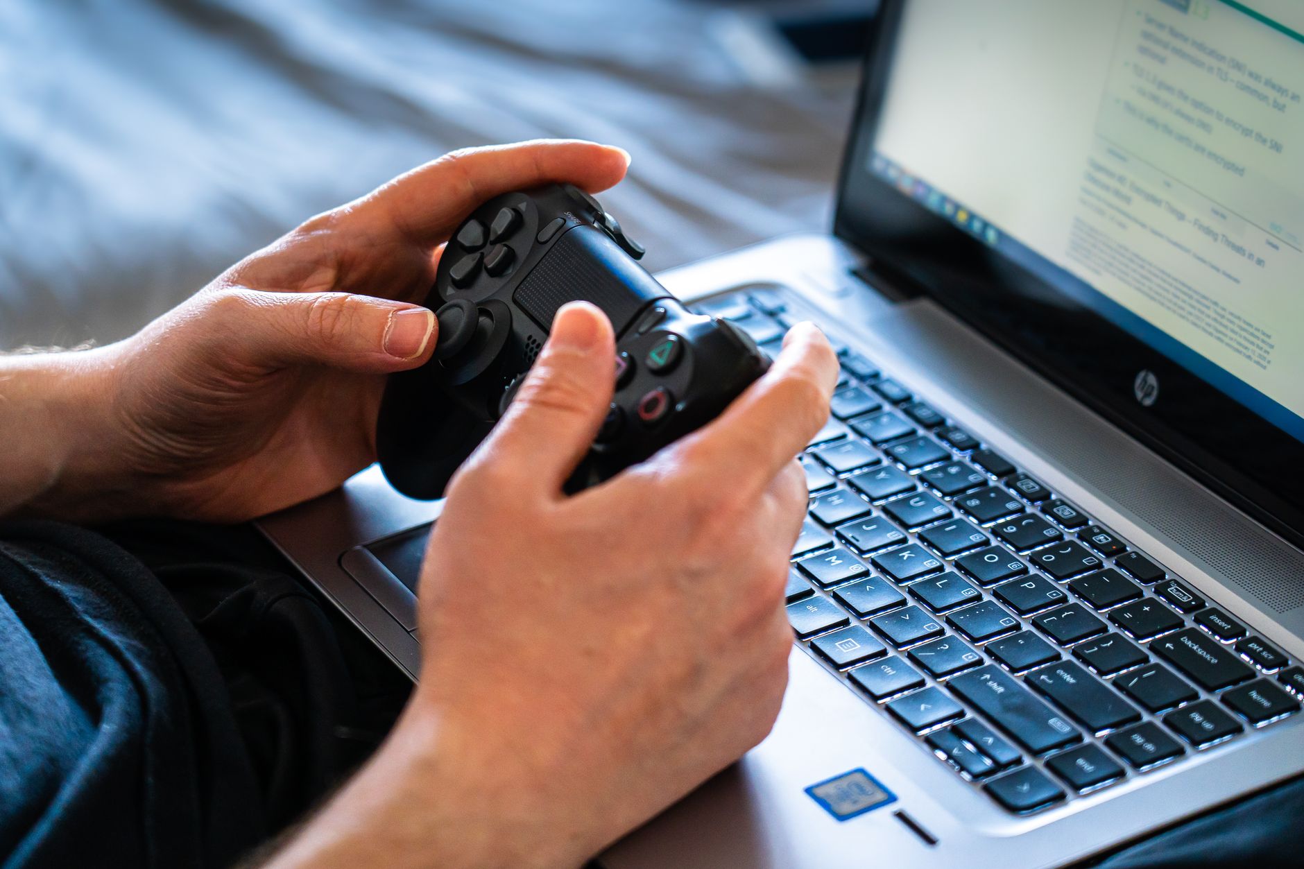 Osoba trzyma pad i korzysta z laptopa podczas grania