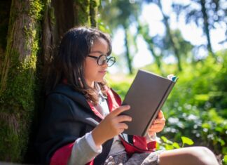 Książki Minecraft dla dzieci – serie, poziom trudności i sugerowany wiek czytelnika Dziewczynka w kostiumie czyta książkę przy omszałym drzewie w lesie